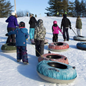 Group of kids and adults pulling tubes up a hill a